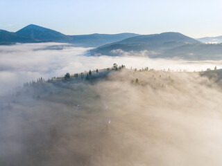 Flight over fog in Ukrainian Carpathians in summer. Mountains on the horizon. A thick layer of fog covers the mountains with a continuous carpet. Aerial drone view.
