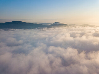 Flight over fog in Ukrainian Carpathians in summer. Mountains on the horizon. Aerial drone view.