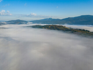 Flight over fog in Ukrainian Carpathians in summer. Mountains on the horizon. A thick layer of fog covers the mountains with a continuous carpet. Aerial drone view.