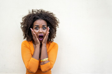 young African woman with hands to her face while screaming in awe and fear, portrait of facial...