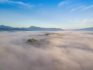 Fototapeta na wymiar Flight over fog in Ukrainian Carpathians in summer. A thick layer of fog covers the mountains with a solid carpet. Mountains on the horizon. Aerial drone view.