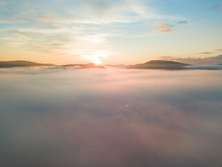 The rays of dawn over the fog in the Ukrainian Carpathians. Aerial drone view.
