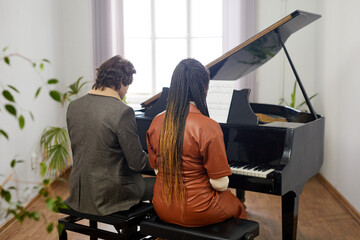Rear view of young couple playing the classical composition on grand piano together at classroom
