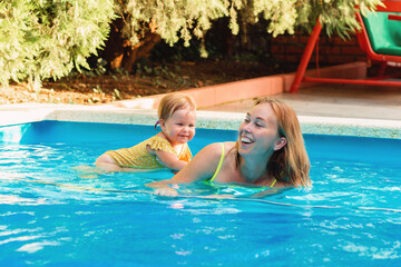 Teaching to swimming. Portrait of happy mother with her little daughter swimming in the pool. Summer activity concept