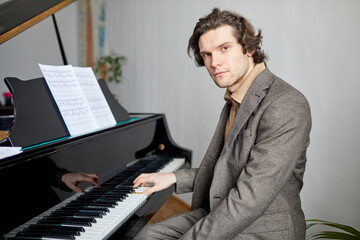 Portrait of professional pianist in suit looking at camera while playing notes on the piano at...