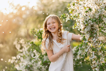 Portrait of laughing girl under falling petals of cherry blossom flowers in spring.