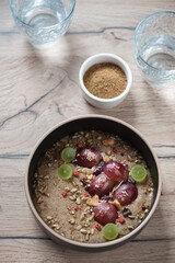 Bowl of flaxseed porridge with grapes on a brown wooden background, vertical shot, elevated view