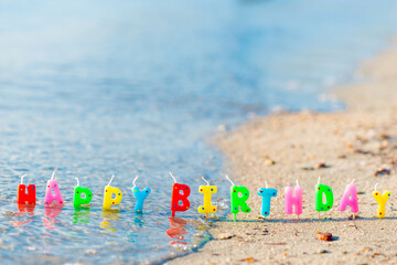 Happy birthday colorful candles on a beach
