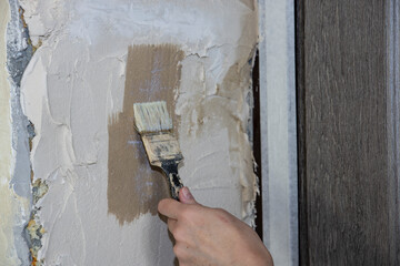 The builder applies soil to the wall. A painter paints the slope of a doorway with a brush, makes...