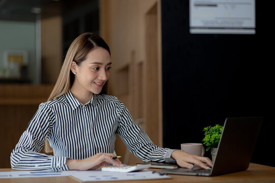 Beautiful Asian young woman looking at information on a laptop, concept image of Asian business woman working smart, modern female executive, startup business woman, business leader woman.