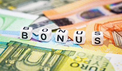 Small white beads with black letters BONUS on euro banknotes, closeup detail