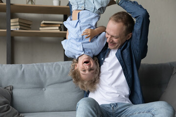 Happy young father lifting in air upside down laughing adorable small kid son, having fun together...