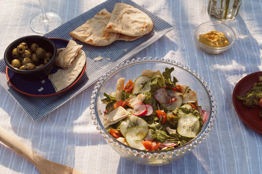 Summer time meal outside arranged on a white table cloth. Salads, breads, olives and drinks. Alfresco food concept image.