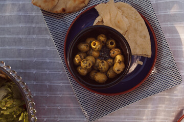 Macro shot of green olives in a bowl with bread. Rustic mezze style food in summer picnic style setting. Alfresco dining food concept image with natural sunlight