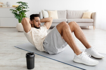 Full length of sporty young Arab man strengthening core muscles, doing abs exercises at home