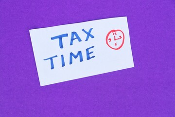 Tax Time Phrase with a Clock Drawn on a Paper Piece Isolated on Blue Background, Money and Financial Conceptual Photo