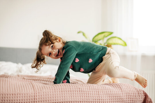 A charming little girl jumps on the bed and laughs