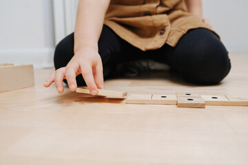 Close up image of a boy sitting on the floor, playing with domino pieces