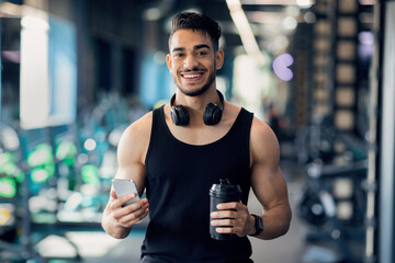Sport App. Cheerful Middle Eastern Male Athlete Posing With Smartphone In Hand