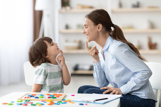 Speech training for kids. Professional woman training with little boy at cabinet, teaching right articulation exercises