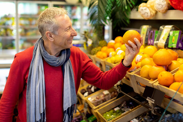 Positive senior man choosing fresh organic fruits at supermarket