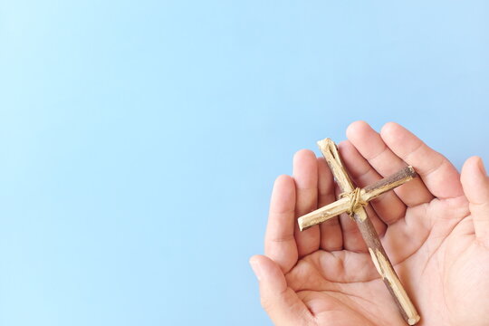 Top view of hand holding wooden cross crucifix with copy space in blue background. Catholicism, Christianity, Thanksgiving, Catholic and Christian faith concept. - Powered by Adobe