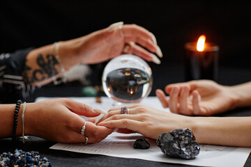 Close up of fortune teller holding hand of young woman during spiritual seance with crystal ball