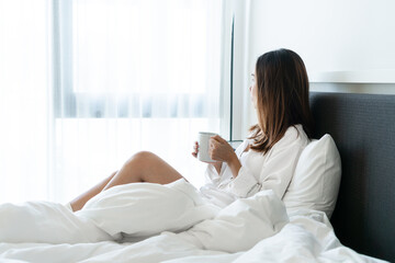 Young beautiful brunette hair female in white shirt pajamas drinking coffee while sitting on the...