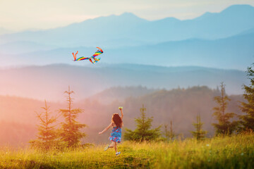 Little happy child girl running with kite. Wonderful mountain landscape in Alps at sunset. Travel,...