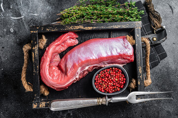 Whole raw veal beef tenderloin in wooden tray. Black background. Top view