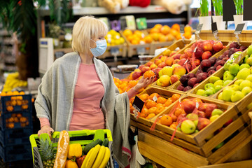 Female customer in face mask choosing fruits at supermarket
