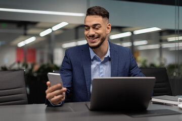 Smiling arabic businessman checking mobile app while working