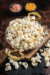 Prepared salty popcorn in a skillet and corn kernel. Dark background. Top view