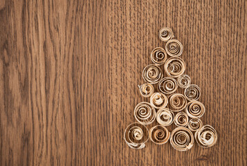 Spruce from wood shavings on a wooden background. Light wooden curls are folded in the form of a Christmas tree. New Year's card from sawdust with a place for text or inscription
