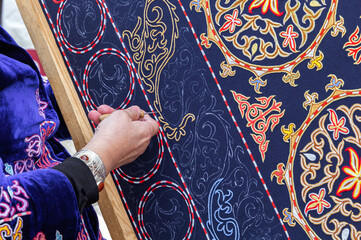 Woman's hand embroiders an Asian ornament on a carpet with gilded thread. Handmade