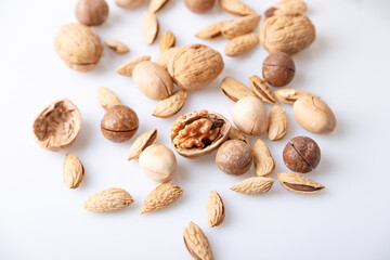 Assorted nuts in the shell on a white background: walnuts, pecans, almonds, macadamia. Selective focus, close-up.