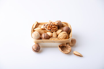 Assorted nuts in the shell on a white background: walnuts, pecans, almonds, macadamia. Nuts in a basket. Selective focus, close-up. Place for text.