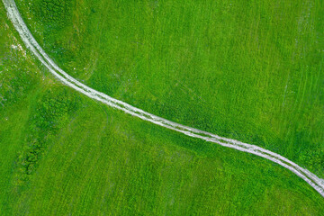 Countryside road across field of green grass, aerial view directly above