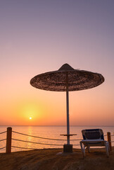 a chaise longue under an umbrella on the background of a sunset on the sea.