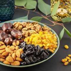 Ramadan concept. Nuts, dried fruits and dates in the blue bowl, glass of water and ramadan lantern on a black background with copy space. Arab dish, sweets. Islamic traditional food. Soft focus