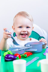 a small child plays children's dishes with vegetables, sitting at the table