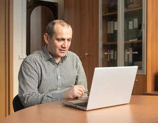 a man participates in a video conference at a laptop in the office