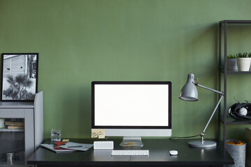 Background image of home office workplace with blank computer screen against green wall, copy space