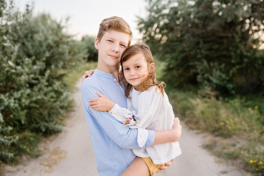 Portrait Of Older Brother And Younger Sister Together Outside. Siblings Enjoying Summertime Outside In The Field. Natural Facial Expression, Minimal Editing Photo