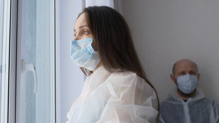 Tired health worker in the rest room dressed in masks, a female nurse adjusts her mask and looks out the window, a male doctor sits and rests after a serious operation with a fatal outcome.