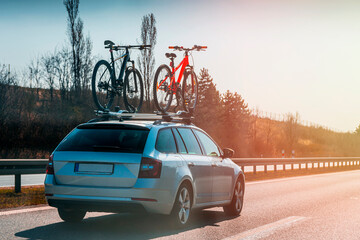 Bicycle roof mount. Car with two bicycle mounted to the roof on the highway at sunny day. Transportation of mountain bikes on the roof of the car.