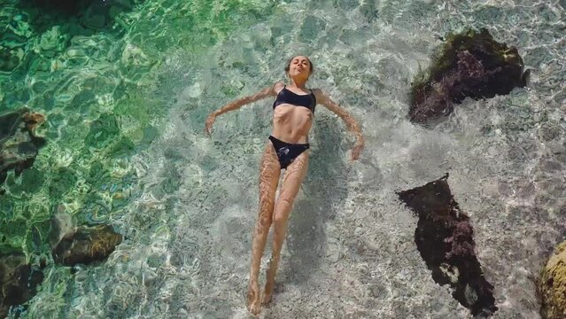 High angle view of relaxing woman in black bikini with perfect body floating in blue clear sea water. Happy island getaway vacation in Turkey