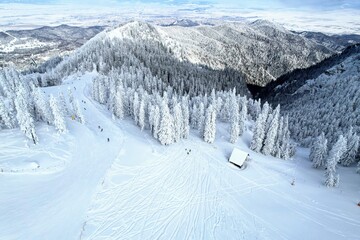 Aerial view of a ski slope in Postavarul massif and of the surrounding mountains and valleys in the distance covered by heavy frozen snow. Brasov, Romania