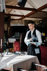 A young male waiter in a stylish uniform is engaged in serving the table in a beautiful gourmet restaurant. A high-level restaurant. Table service in the restaurant.