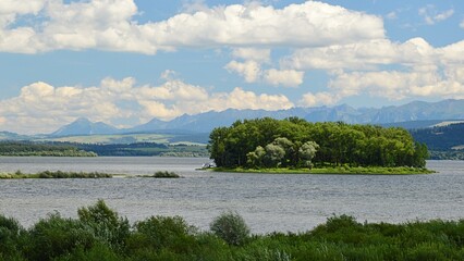 Landscape with Slanica Island Of Art in center of Orava river dam in northern Slovakia covered with mostly broadleaf trees, during beautiful partially cloudy summer day.